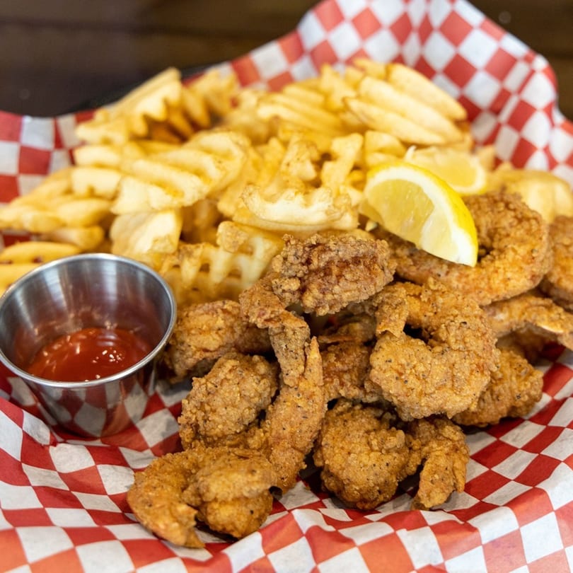 Seafood Palace's fried shrimp and waffle fries with a lemon wedge and ketchup in a red checkered basket.