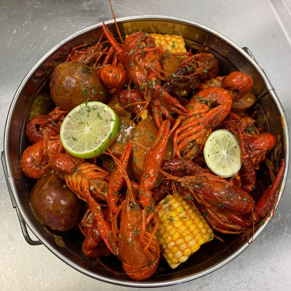 A large metal pot overflowing with boiled crawfish, corn on the cob, potatoes, and lime slices.