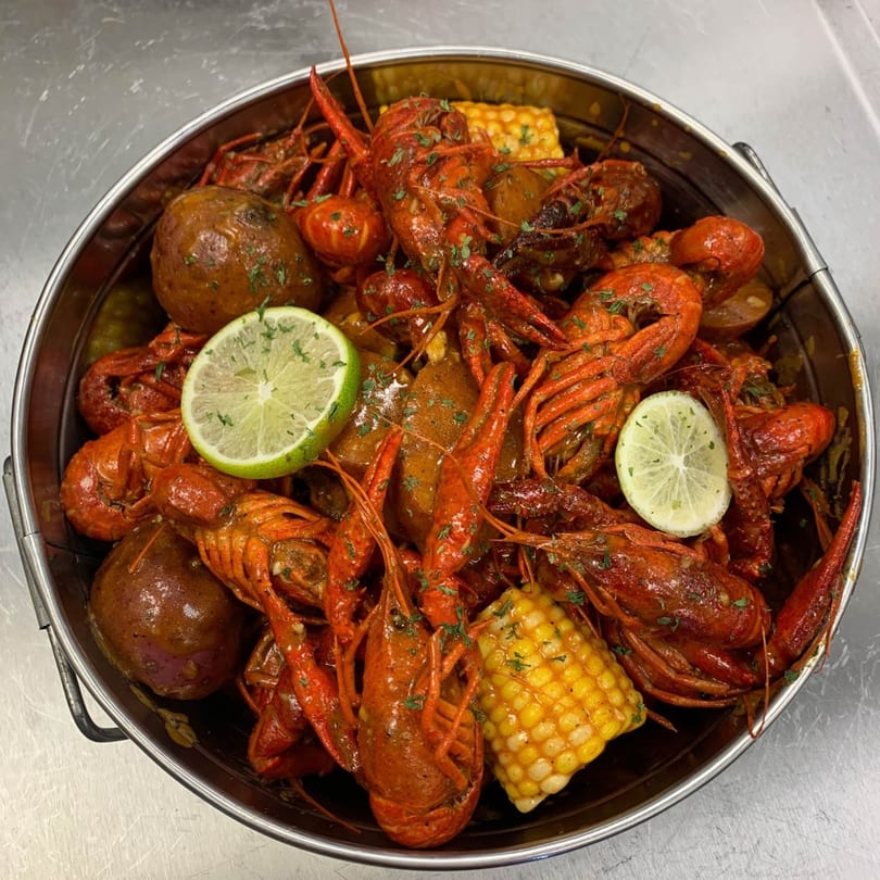A large metal pot overflowing with boiled crawfish, corn on the cob, potatoes, and lime slices.