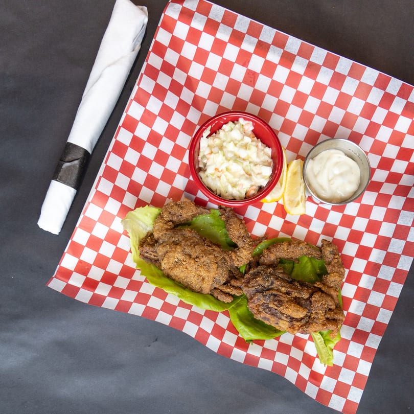 Fried soft-shell crabs on lettuce with coleslaw, mayonnaise, and lemon wedges on red checkered paper.