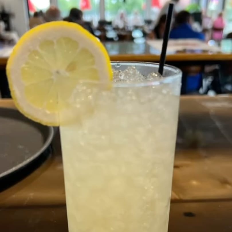 A refreshing drink with ice and a lemon slice, with a blurred restaurant background.