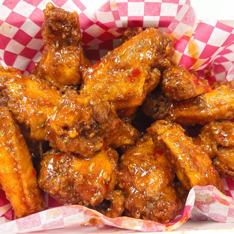 Close-up of crispy, glazed chicken wings with herbs and red pepper flakes in a red and white checkered basket.